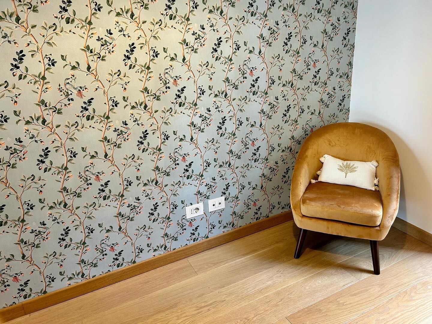 Una poltrona color cuoio in un angolo accanto alla carta da parati con un motivo floreale, con pavimento in legno chiaro.