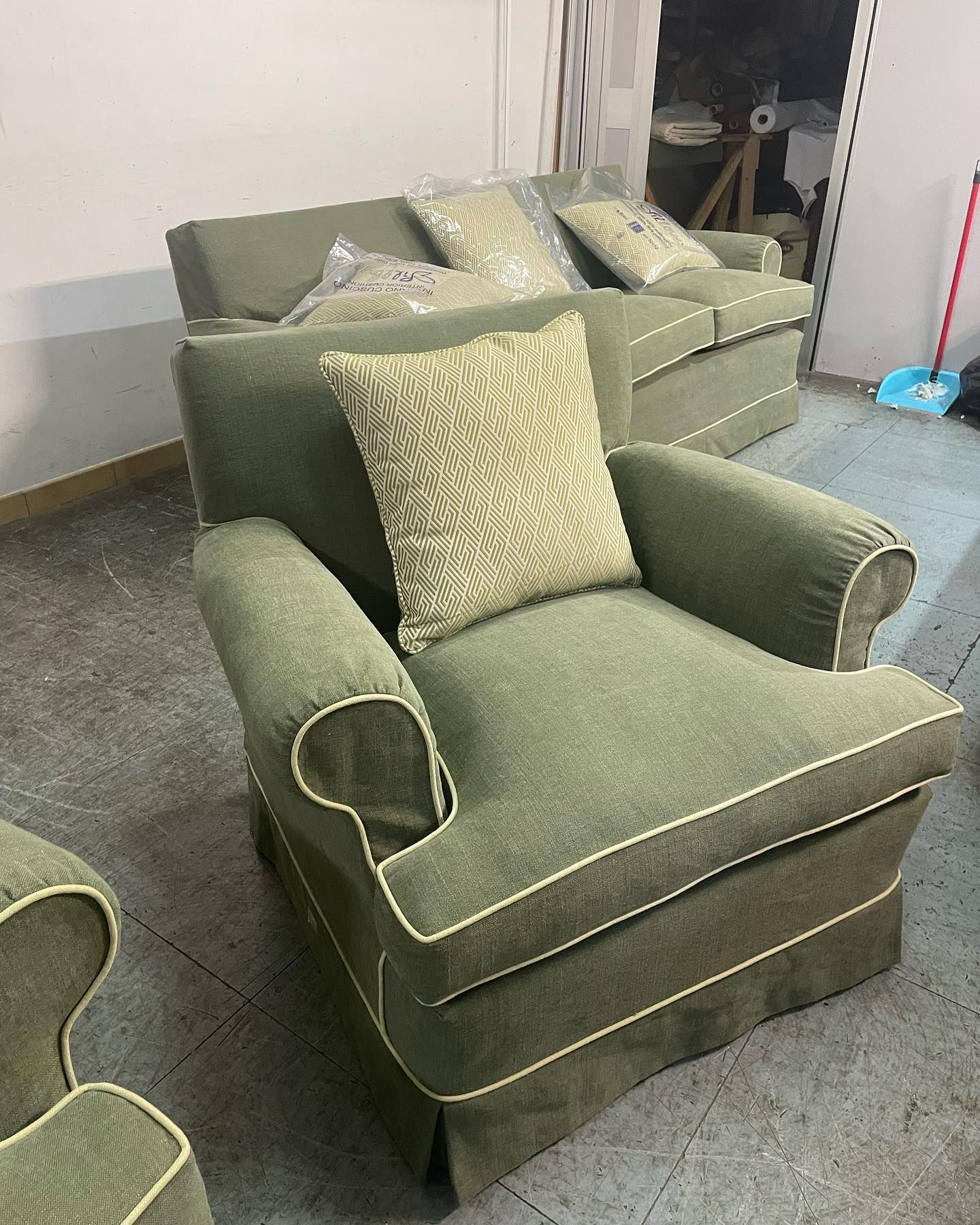Poltrona e divano imbottiti di colore verde con finiture bianche, cuscino decorativo.