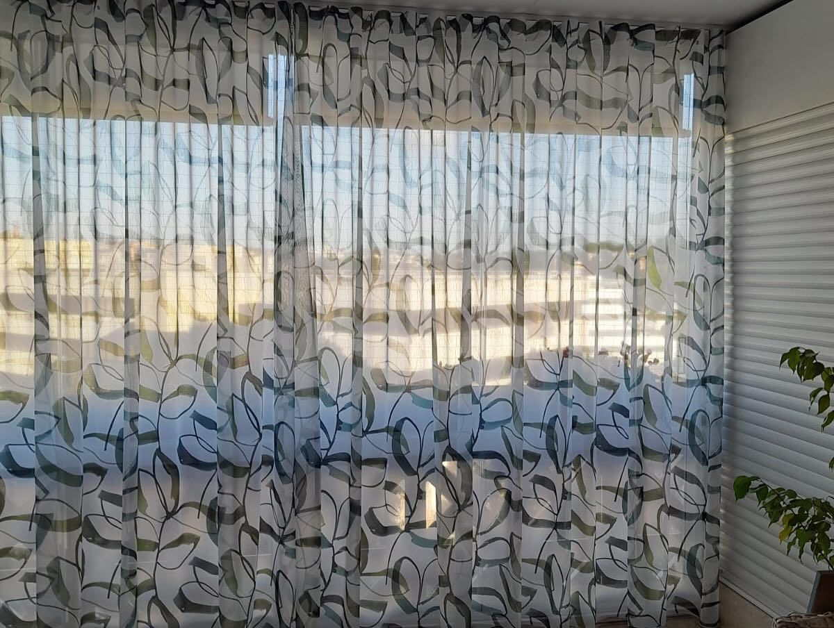 Tende trasparenti con motivi a foglie appese davanti a una finestra, che proiettano ombre.
