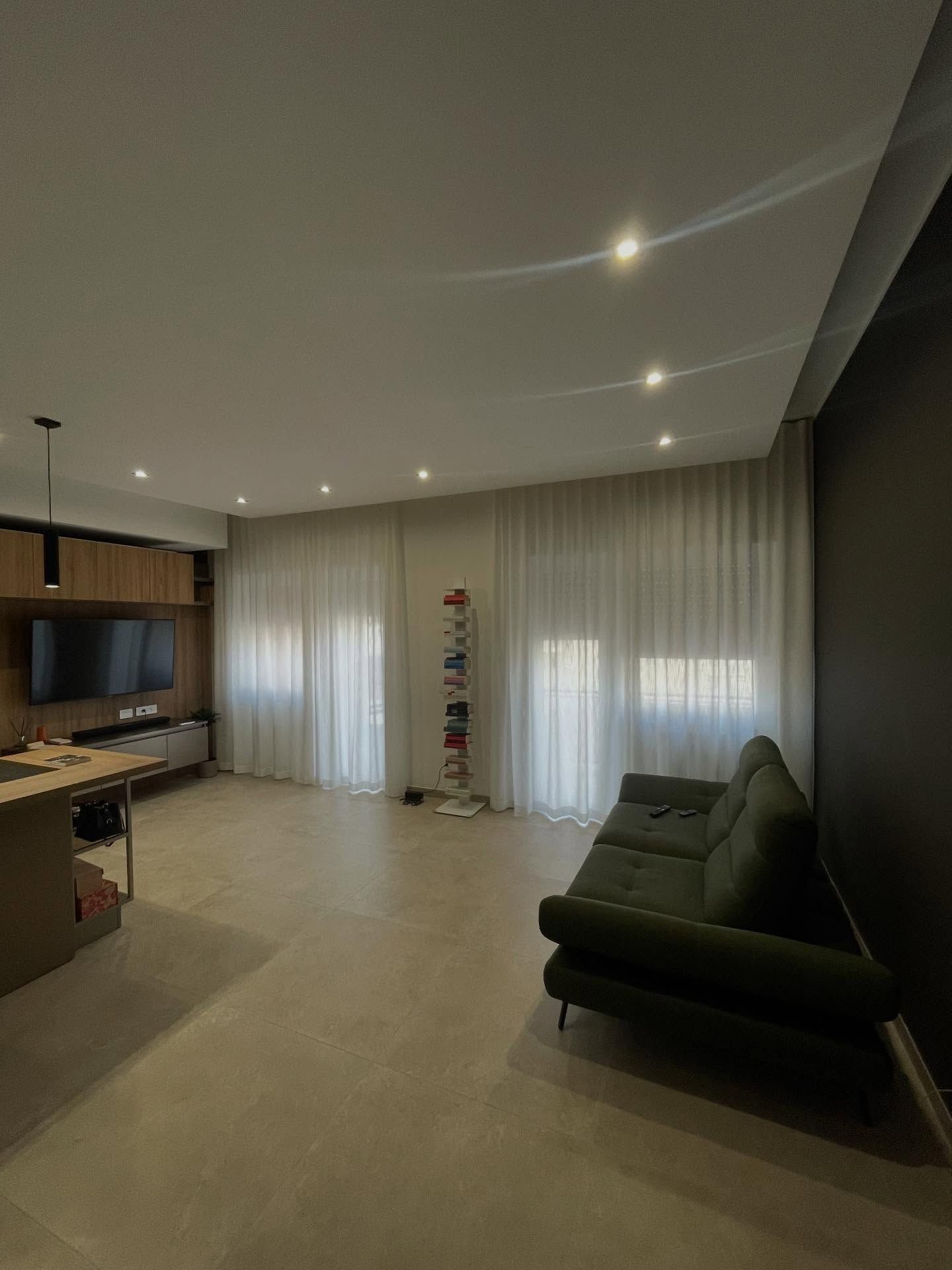 Soggiorno moderno con divano verde, TV su mobile in legno e tende bianche trasparenti.