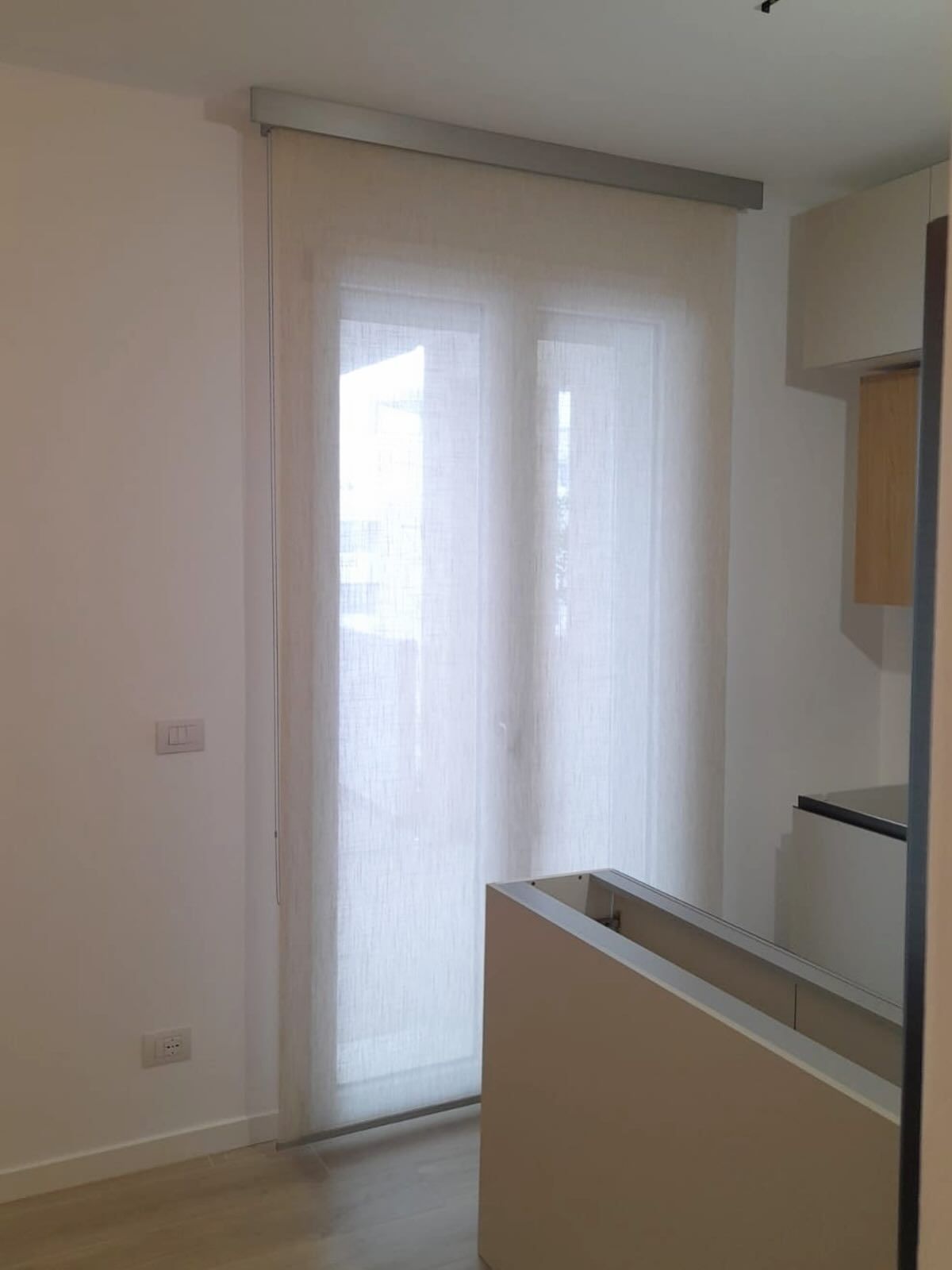 Tende bianche trasparenti sopra una finestra, luce che entra a fiotti. Pareti dai colori neutri, interni contemporanei.