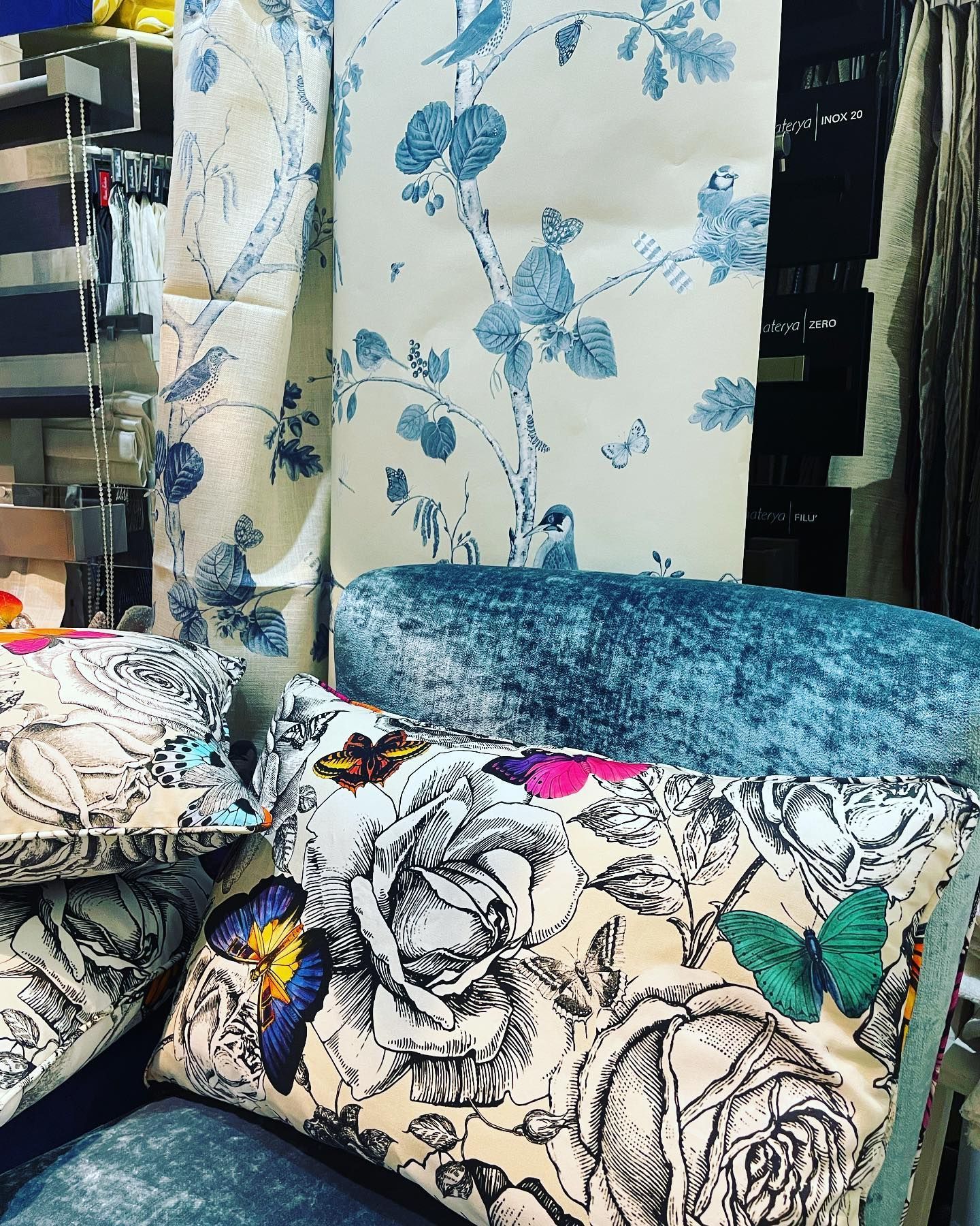 Campioni di tessuto con motivi floreali e di uccelli blu, oltre a cuscini con rose e farfalle.