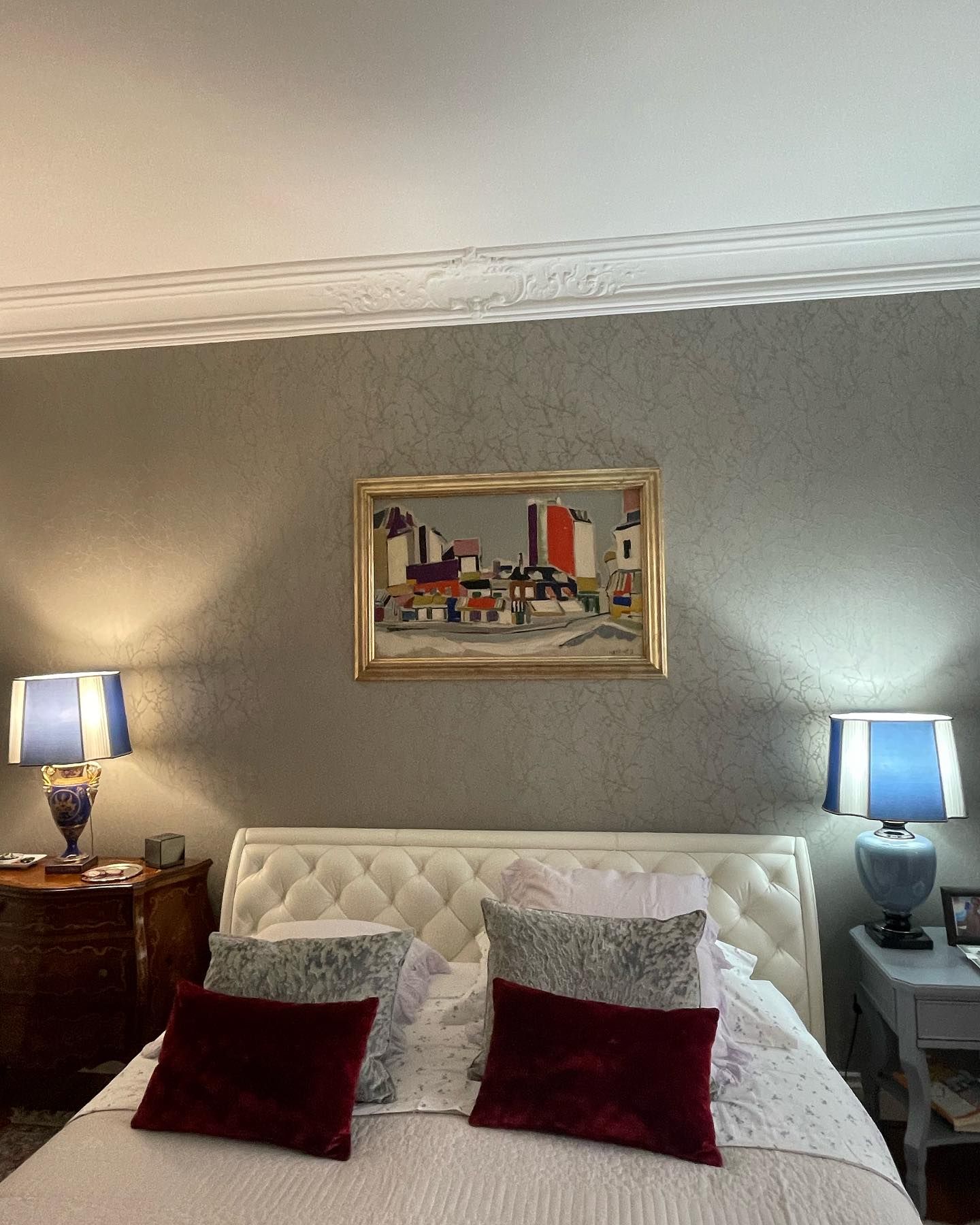 Camera da letto con testiera bianca trapuntata, quadri incorniciati e lampade sui comodini.