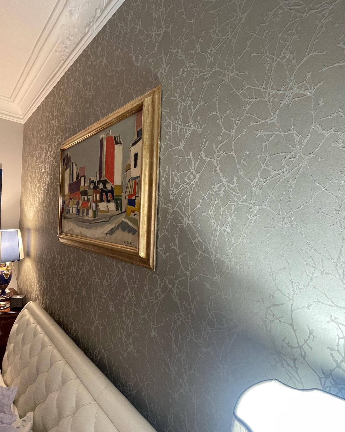 Parete grigia testurizzata con un dipinto con cornice dorata raffigurante una scena cittadina.