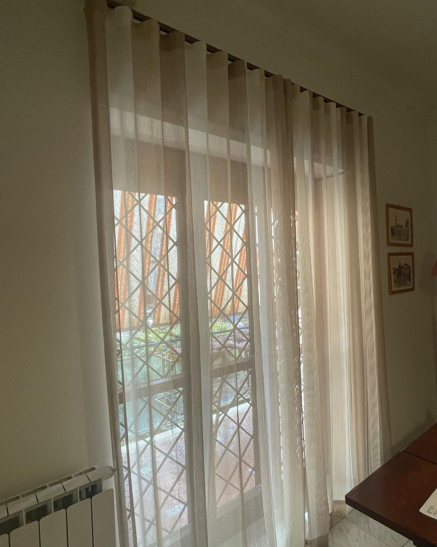 Finestra con tende beige trasparenti, che si affaccia su una finestra a graticcio.