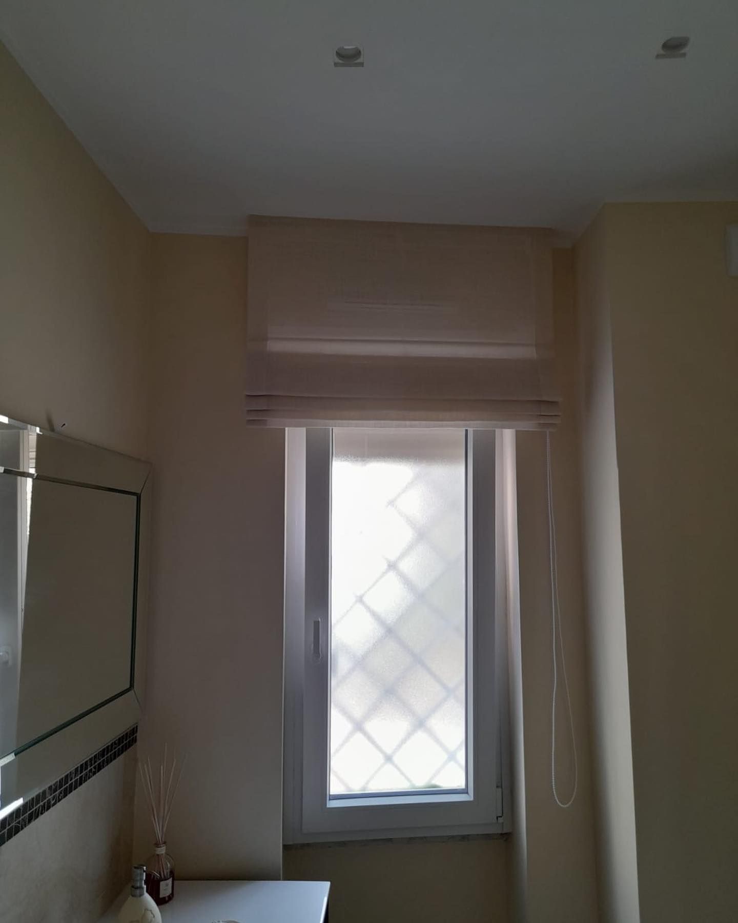 Finestra con persiana romana color crema sopra una finestra con cornice bianca. Le pareti sono di colore beige.