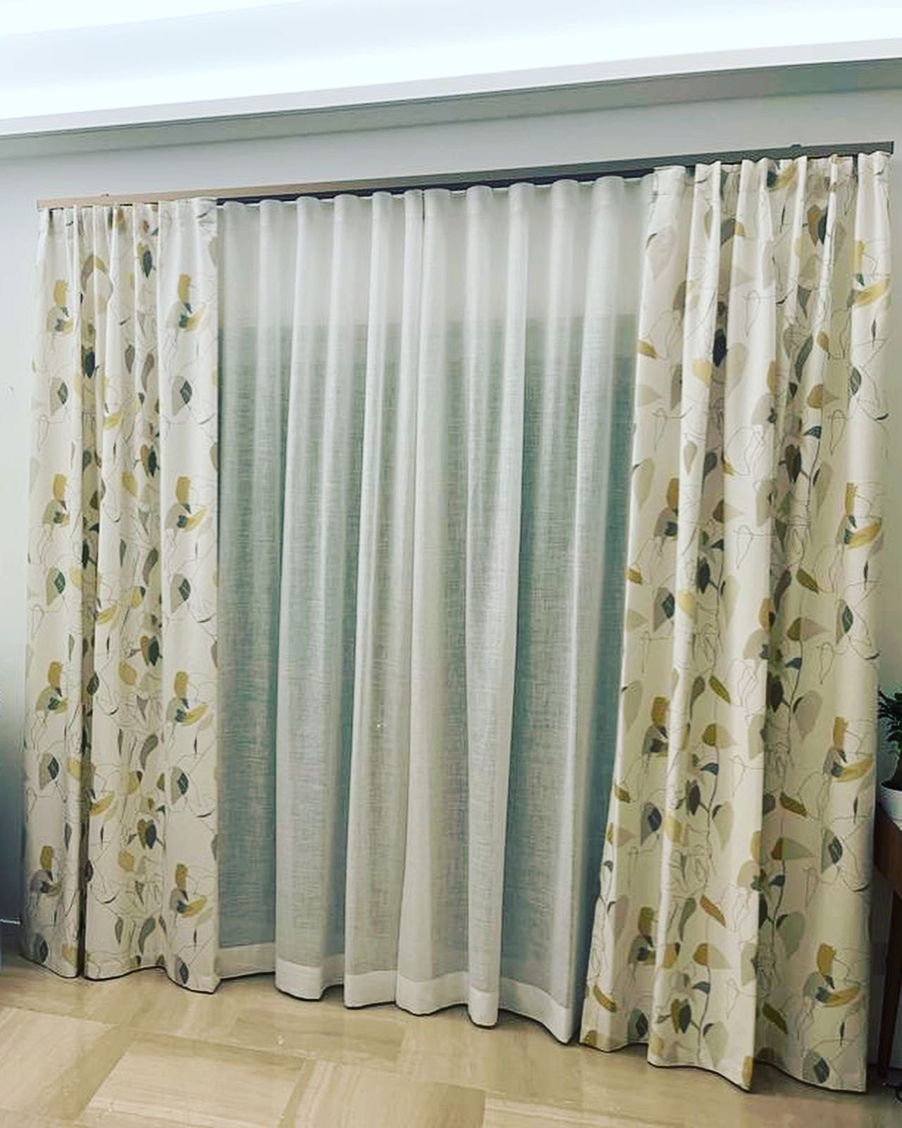 Tende in una stanza. Tende trasparenti color bianco crema affiancate da drappi beige e verdi a fantasia, appese a un'asta.