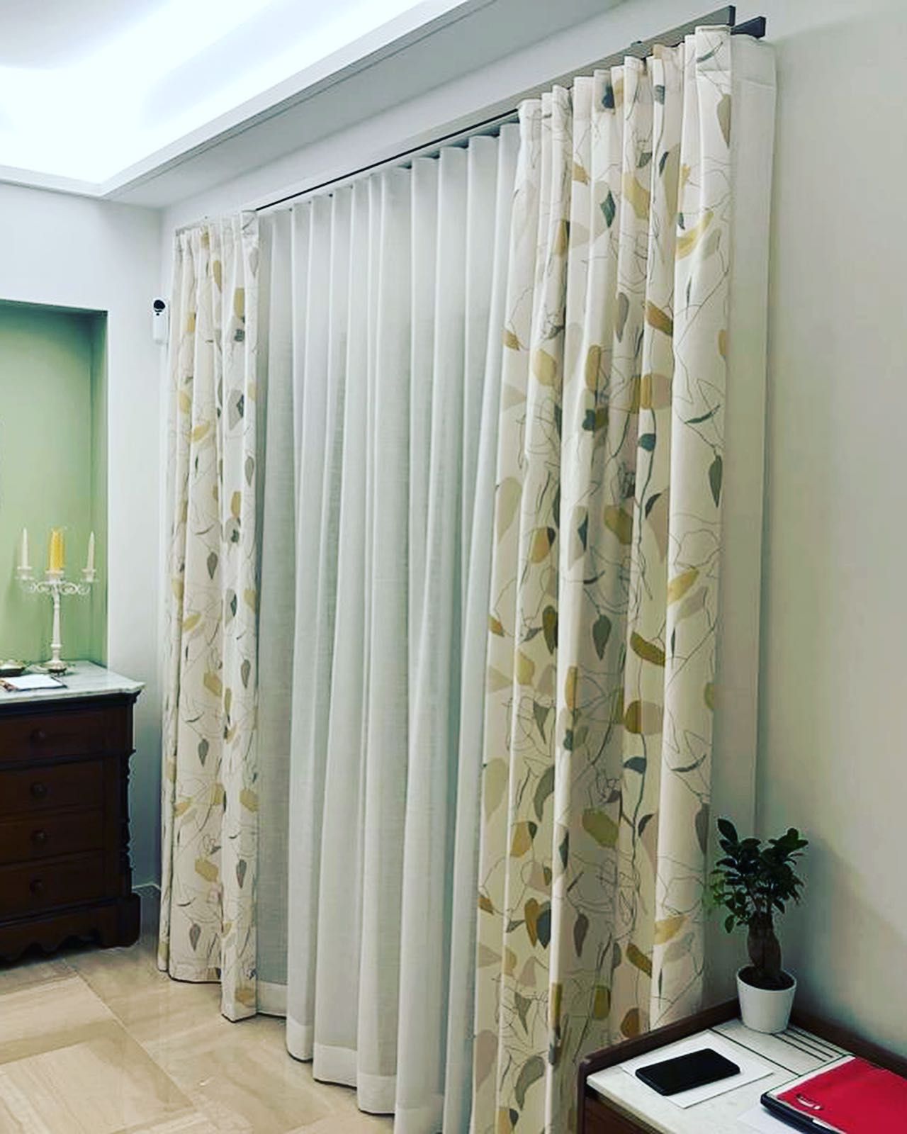 Tende: tende trasparenti color crema e tende a fantasia con motivi a foglia verde/oro, appese a un binario in una stanza.