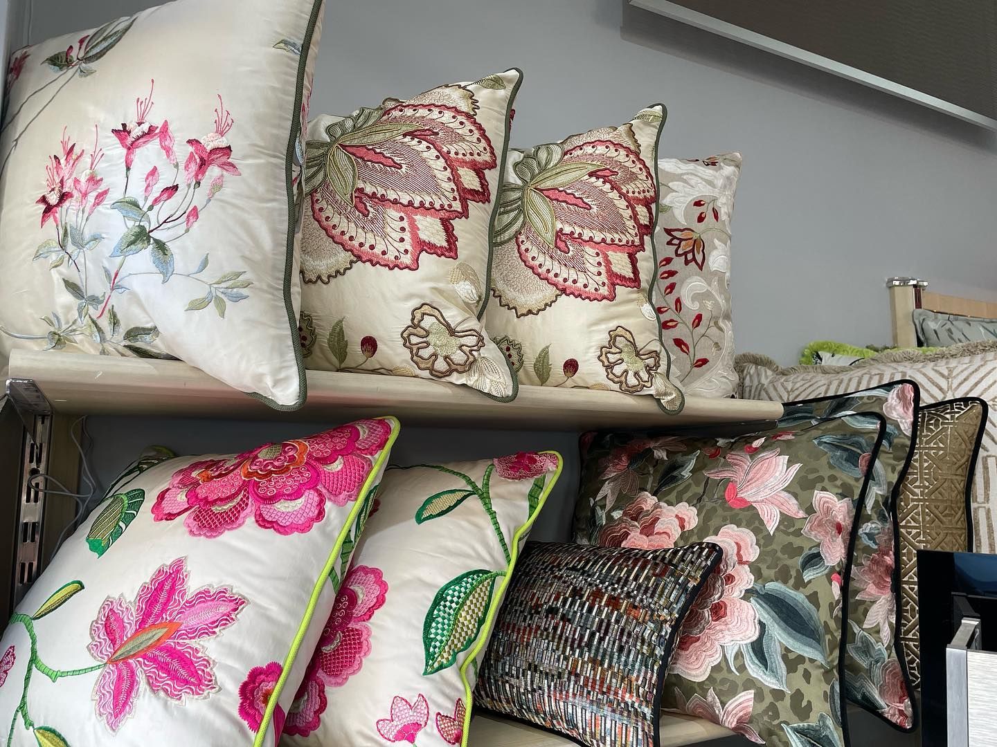 Scaffali con cuscini decorativi a motivi floreali in vari colori, tra cui rosa, rosso, verde e crema.