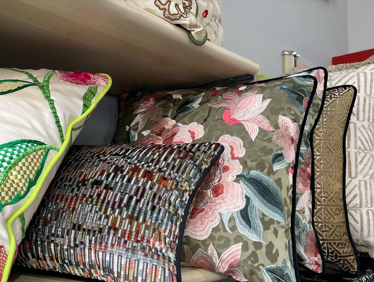 Su uno scaffale sono esposti cuscini con motivi diversi, tra cui motivi floreali e fantasie.