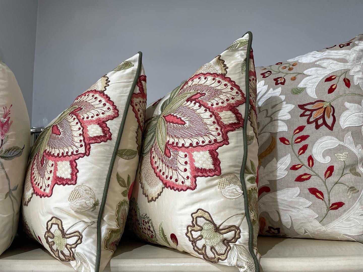 Cuscini decorativi color crema con ricami floreali e rifiniture verdi.