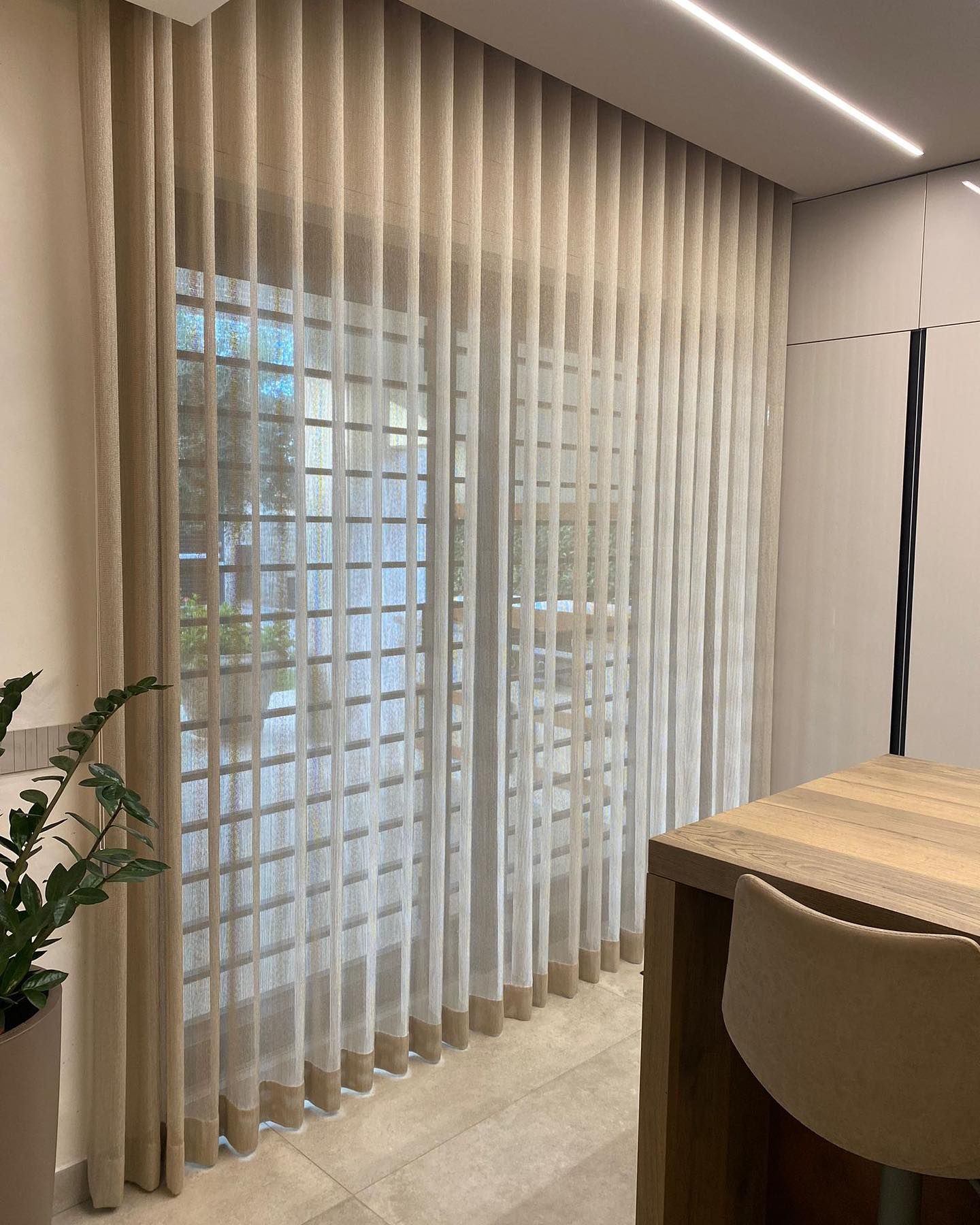 Tende trasparenti beige su una finestra, accanto a un tavolo da pranzo.