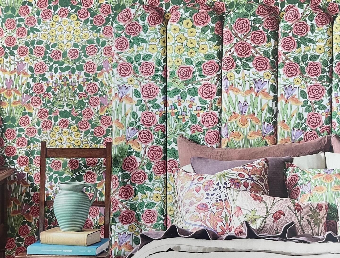 Camera da letto con carta da parati e biancheria da letto a fiori, vaso su una pila di libri, sedia di legno.
