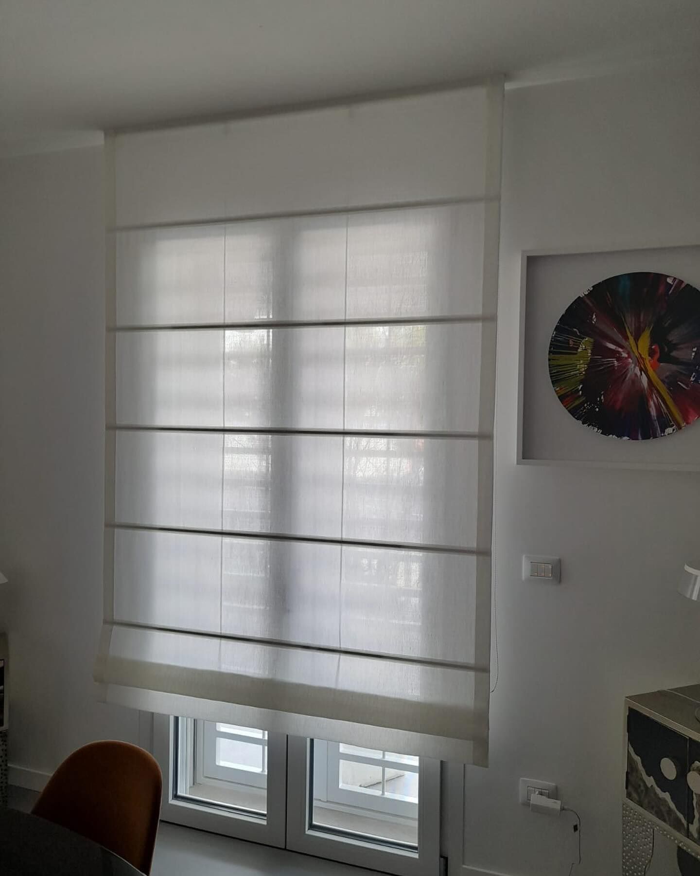 Tenda romana bianca che copre una finestra; opera d'arte su una parete bianca lì vicino.