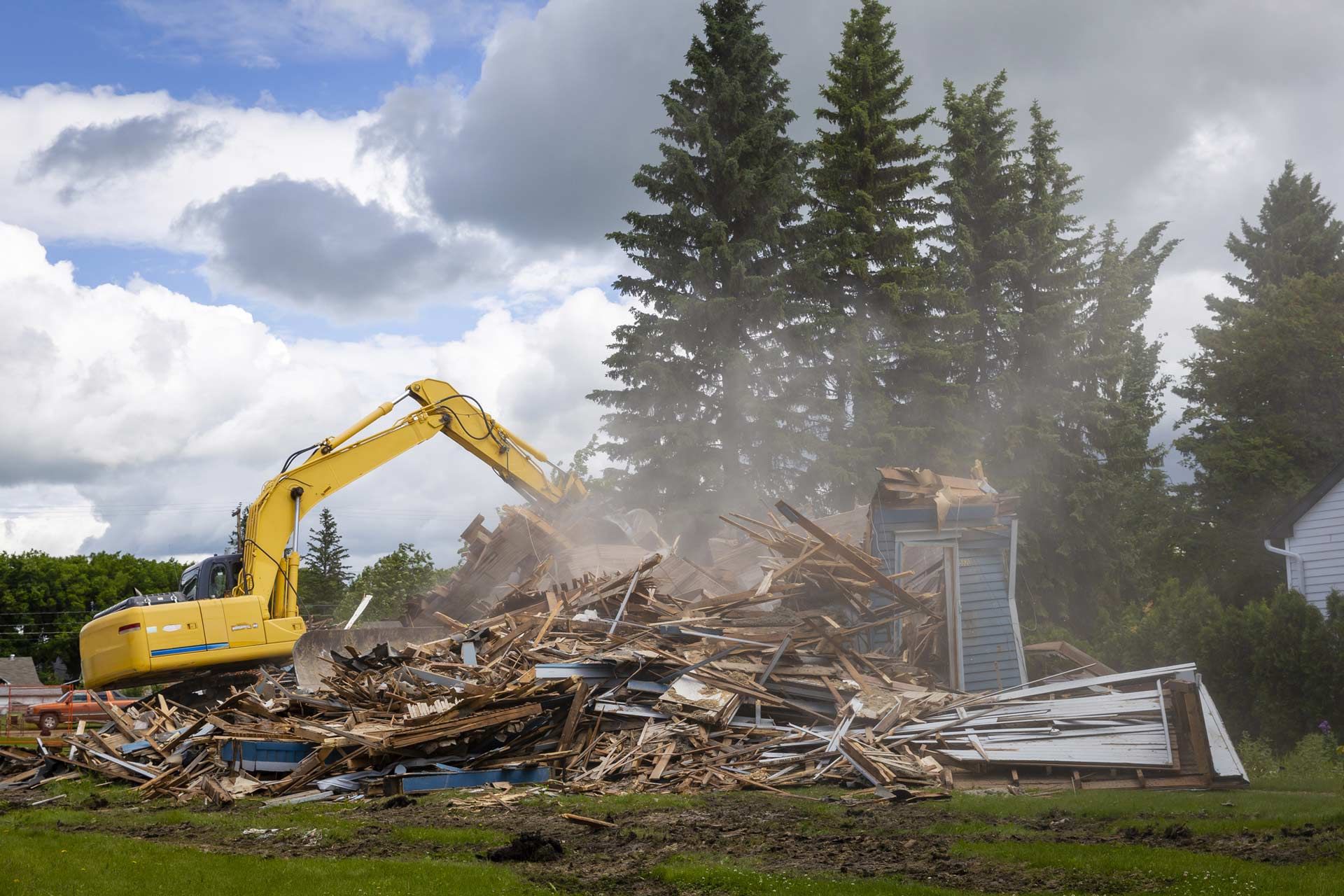 A yellow excavator is demolishing a house in a field.