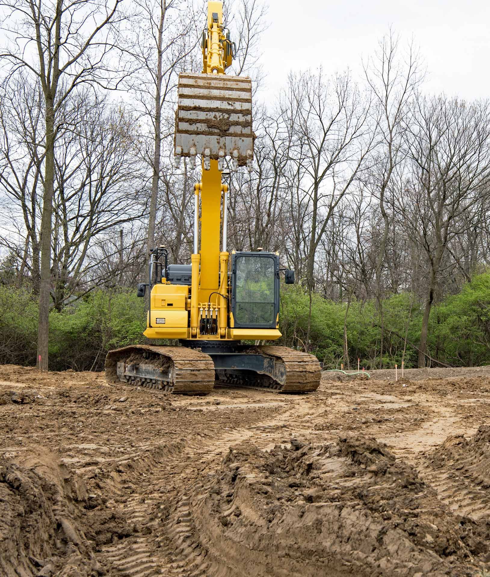 A yellow excavator is sitting in the middle of a dirt field.