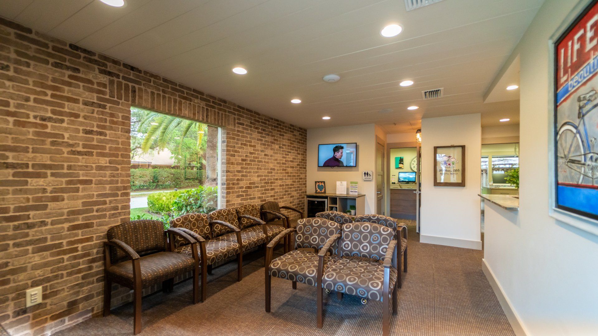 A waiting room with chairs , a television and a brick wall.