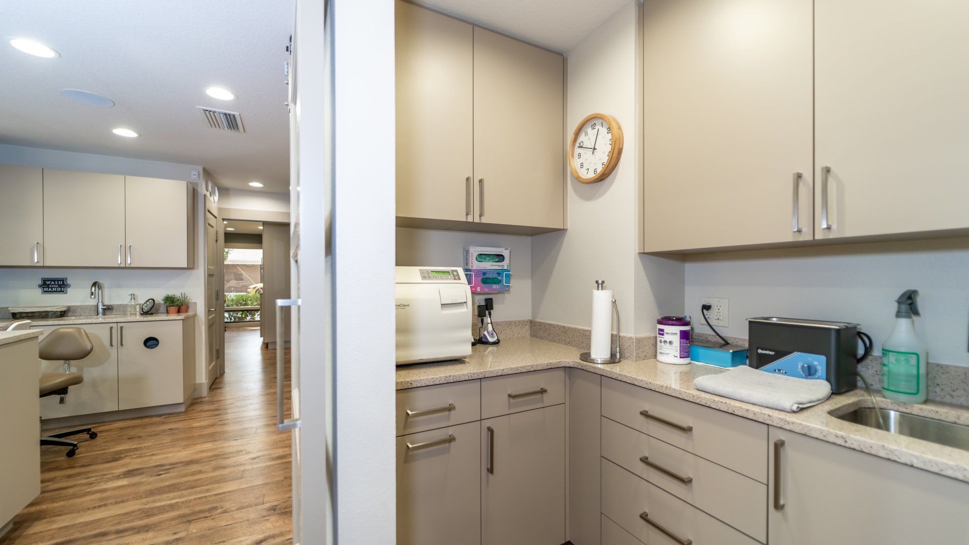 A kitchen with a sink , cabinets and a clock on the wall.