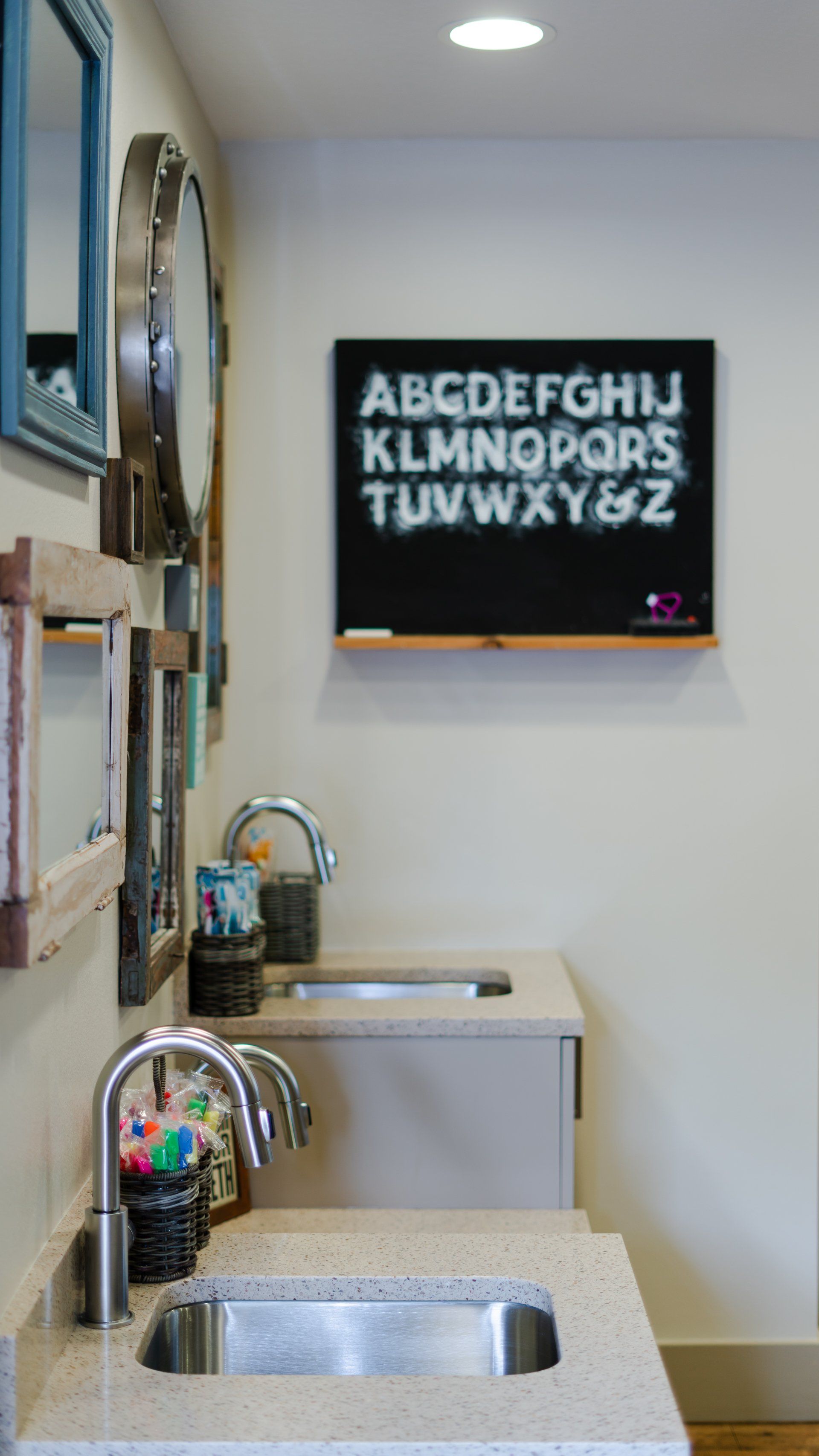 A bathroom with two sinks and a blackboard with the alphabet on it.