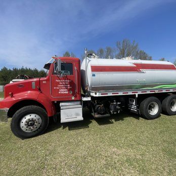 A red and white tanker truck is parked in a grassy field.