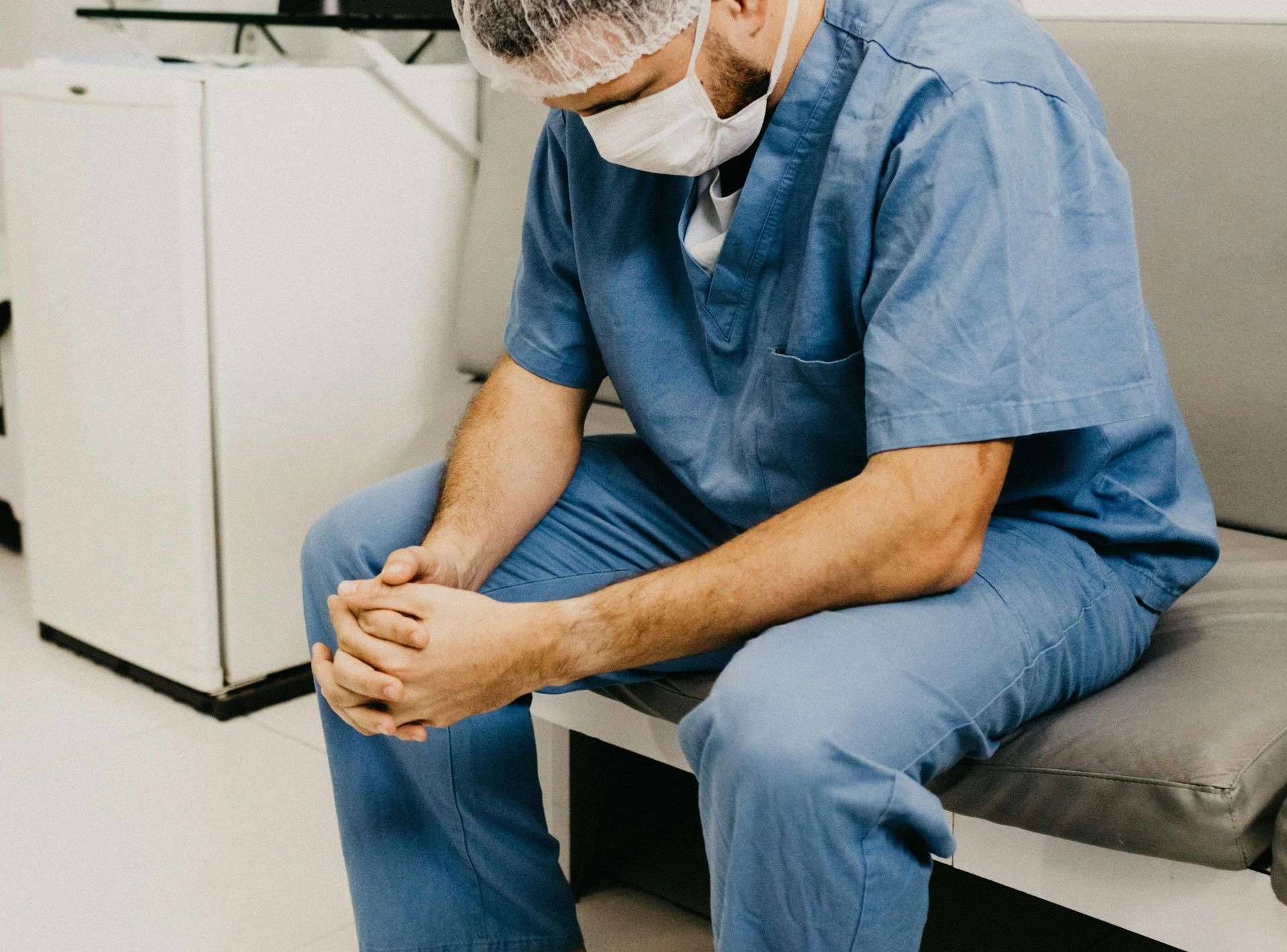 A surgeon wearing a mask is sitting on a couch.