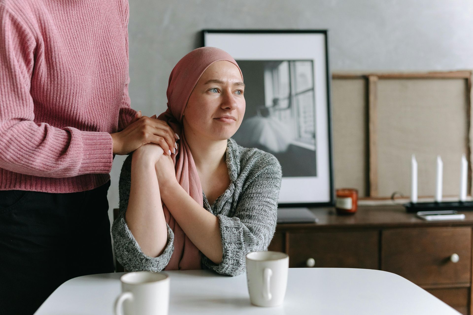 A woman with cancer is sitting at a table with a man standing behind her.