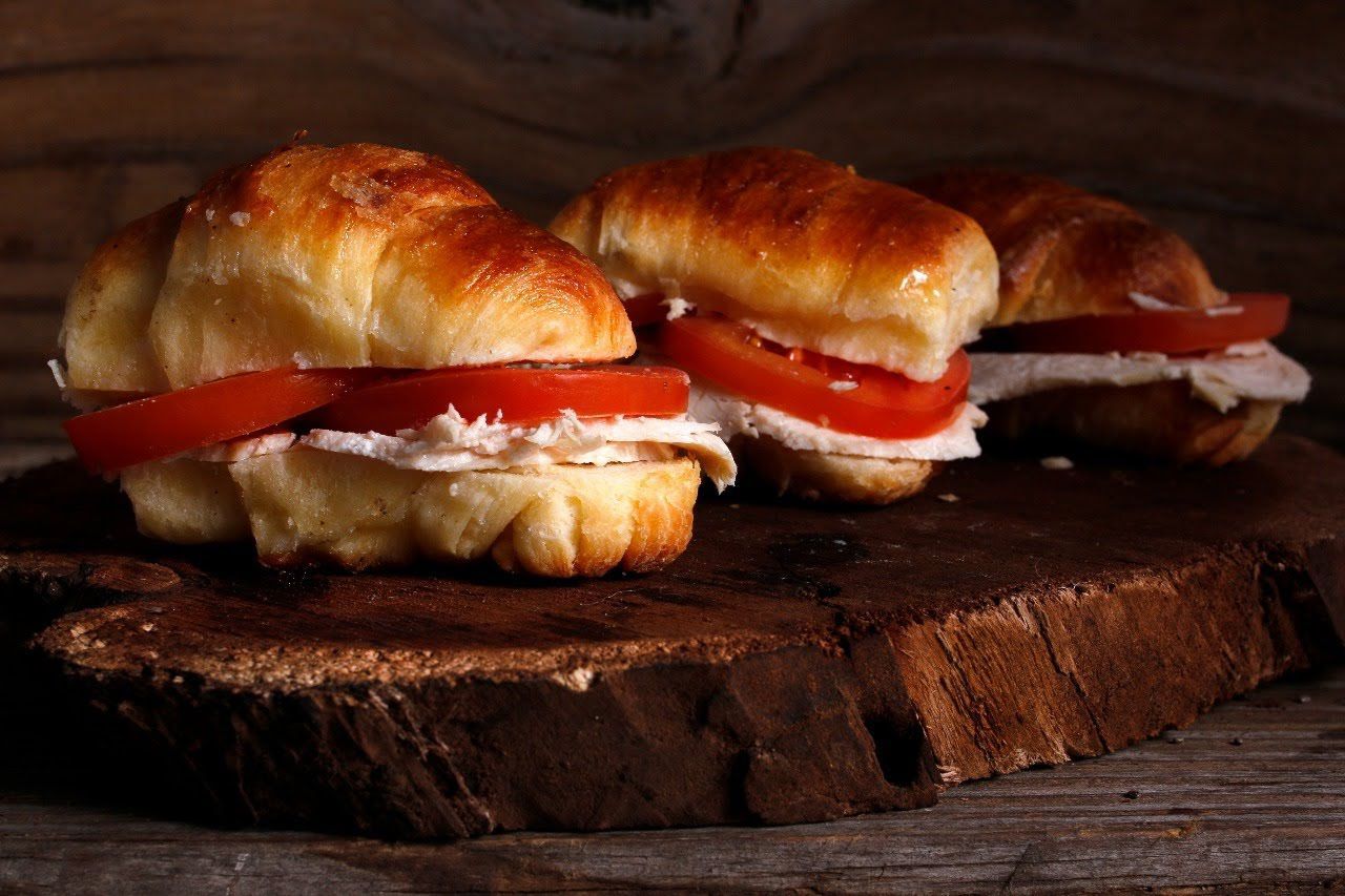 Tres sándwiches de tomate y queso crema en una tabla de madera rústica.