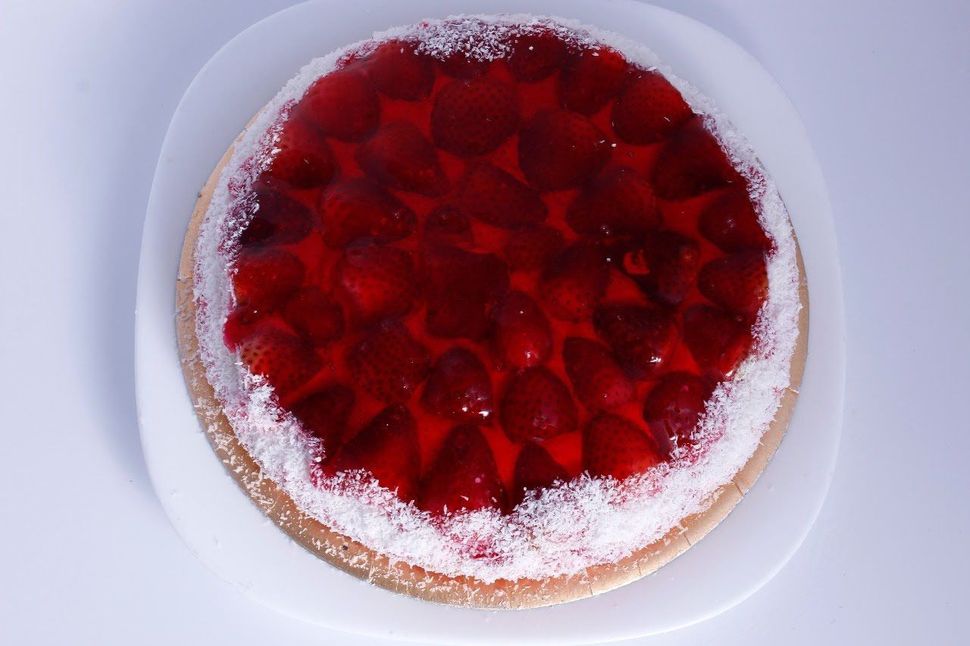 Tarta redonda de frutos rojos con cobertura roja brillante y azúcar glas sobre un plato blanco.