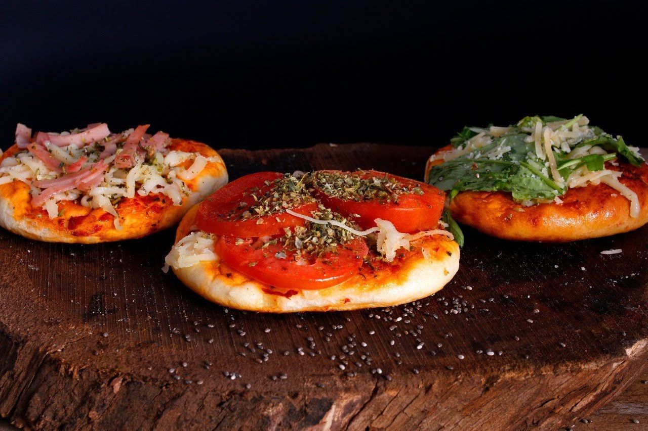 Tres mini pizzas sobre una tabla de madera, cubiertas con salsa de tomate, queso y hierbas.