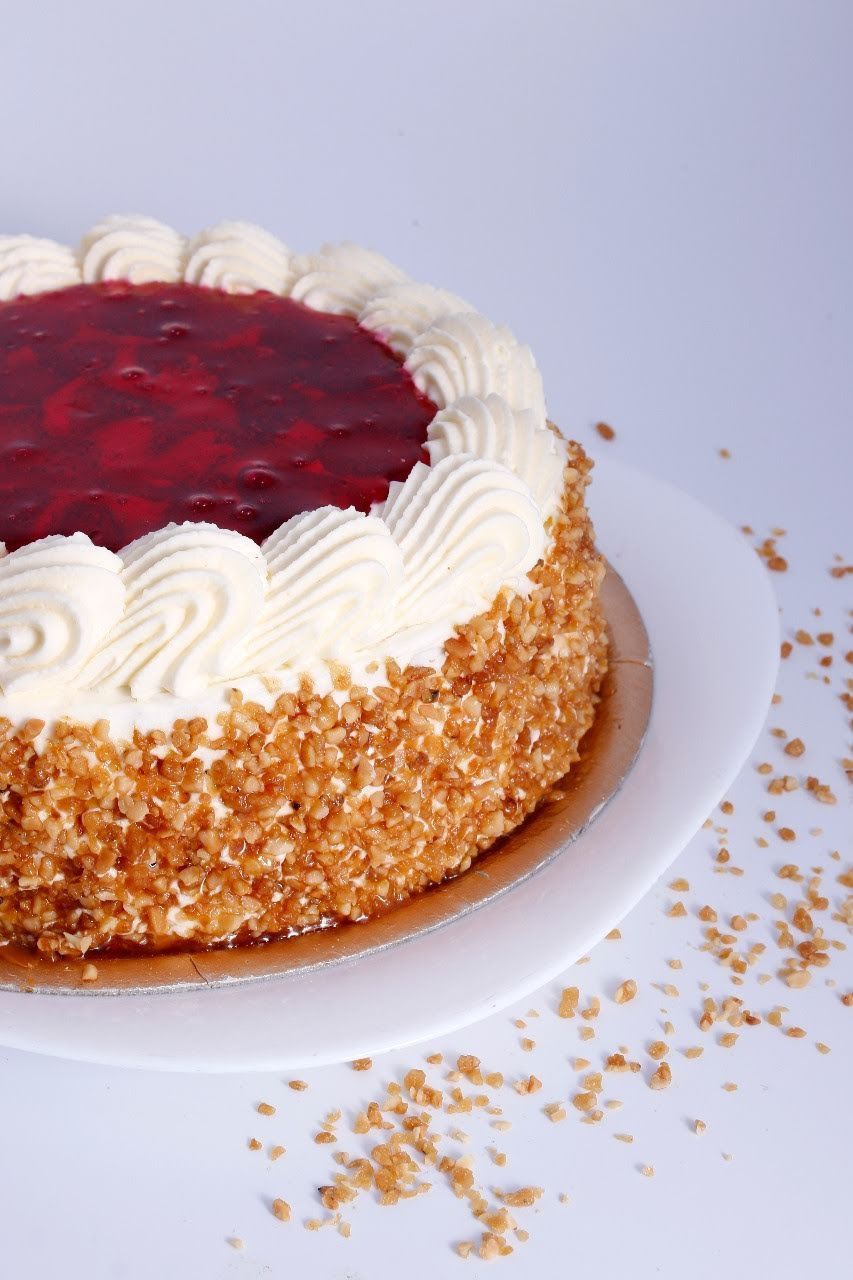 Pastel con glaseado blanco, cobertura de frutos rojos y laterales rebozados con migas, servido en un plato.