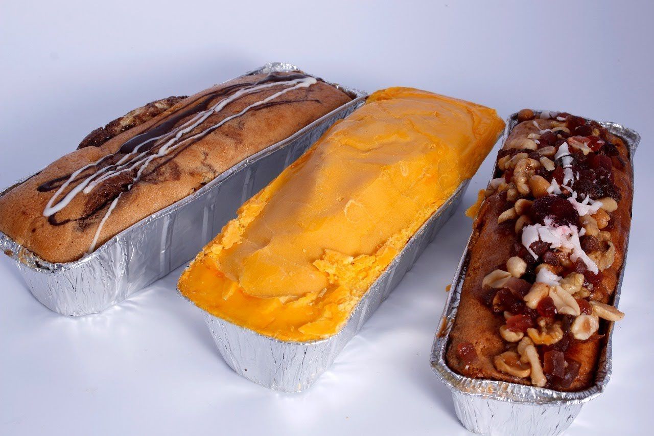 Tres moldes de aluminio para pan con pasteles o panes variados, incluyendo panes bañados en chocolate.