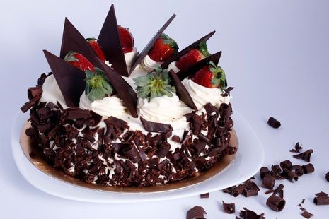 Pastel de chocolate cubierto con crema batida, fresas y virutas de chocolate negro sobre un plato blanco.