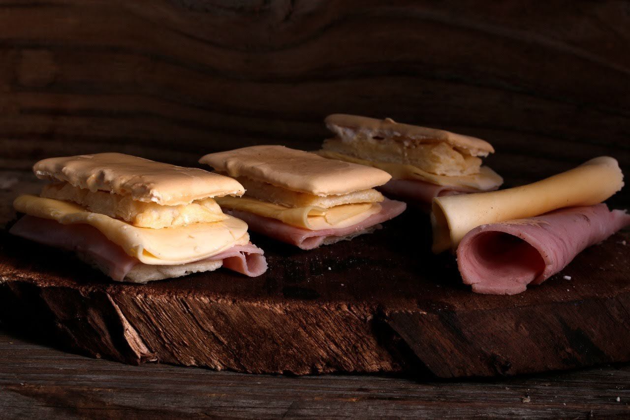 Bocadillos de jamón y queso en pan rústico sobre una mesa de madera oscura.
