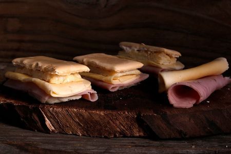 Bocadillos de jamón y queso en pan rústico sobre una mesa de madera oscura.