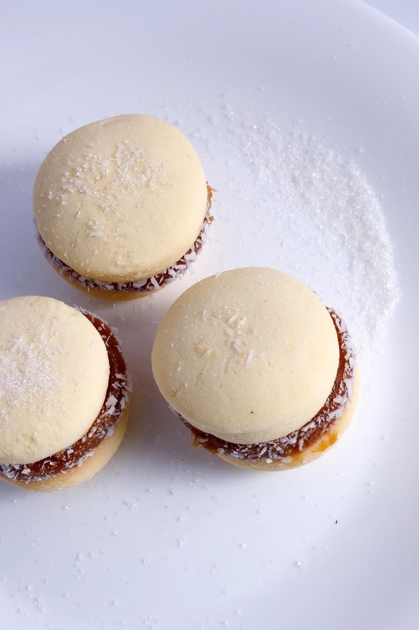 Tres galletas sándwich espolvoreadas con azúcar glas en un plato blanco, una de ellas parcialmente fuera de plano.
