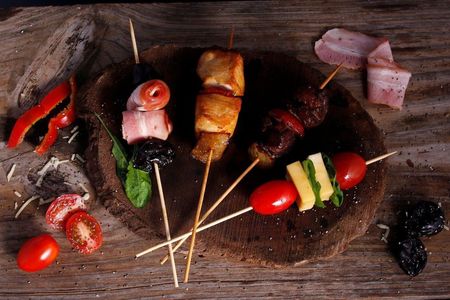 Surtido de brochetas a la parrilla y verduras sobre una tabla de madera rústica, con hierbas y pimientos.