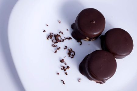 Tres trufas de chocolate en un plato blanco con migas de chocolate esparcidas.