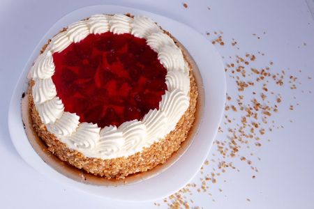 Pastel redondo con centro de gelatina roja, borde de crema blanca y cobertura de migas sobre un plato blanco.