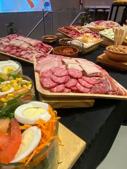 Mesa de buffet con una variedad de carnes en rodajas, ensaladas y guarniciones en bandejas negras.