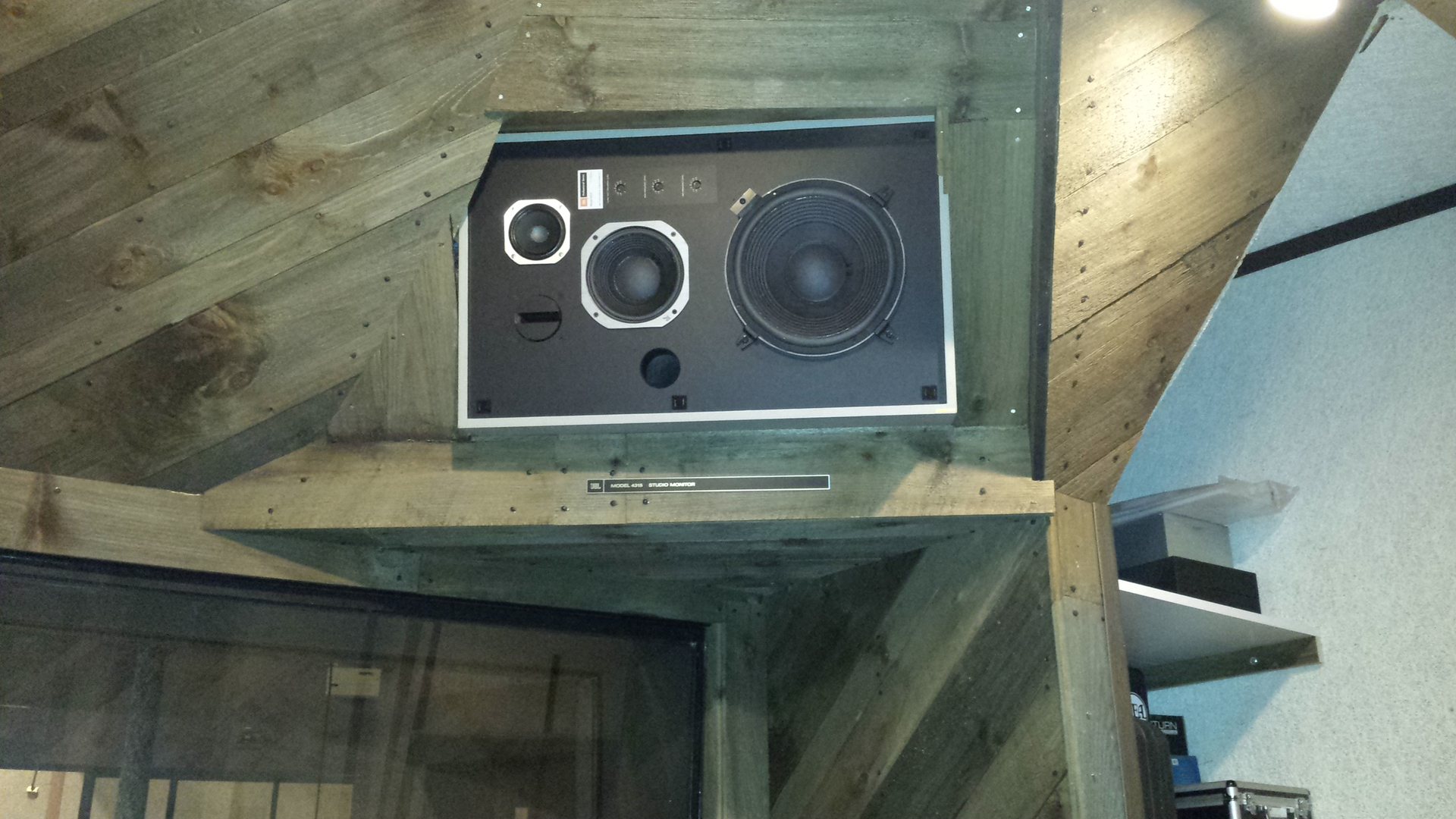 A three-way speaker mounted in a recessed, triangular wooden alcove against a slanted ceiling.