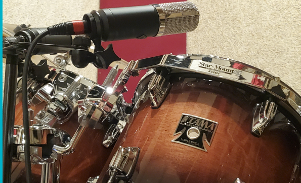 Close-up of a wooden Tama drum with a microphone positioned above it in a recording studio setting.