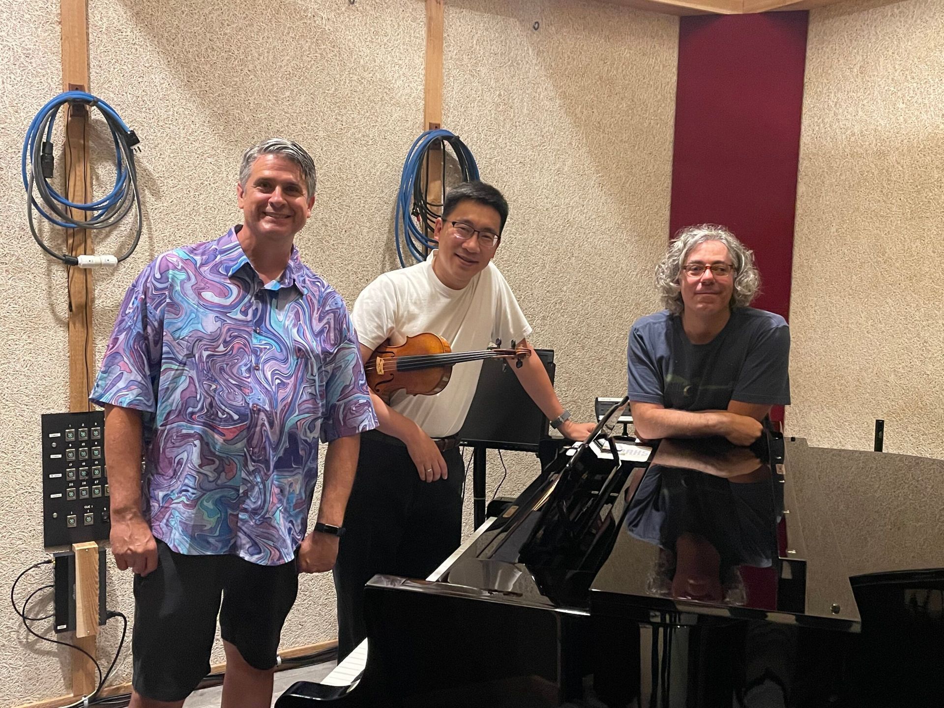 Two wicker chairs with cream cushions and microphones face a small coffee table against a backdrop of red curtains.