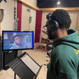A person wearing headphones looks at a screen displaying a video call inside a music recording studio.