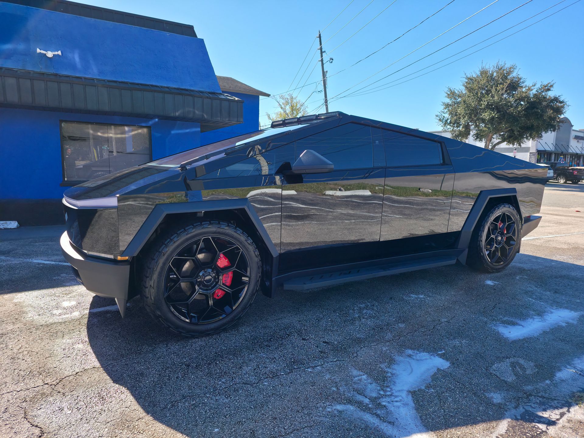 Tesla Cybertruck with black wheels and tinted windows parked outside a blue building.