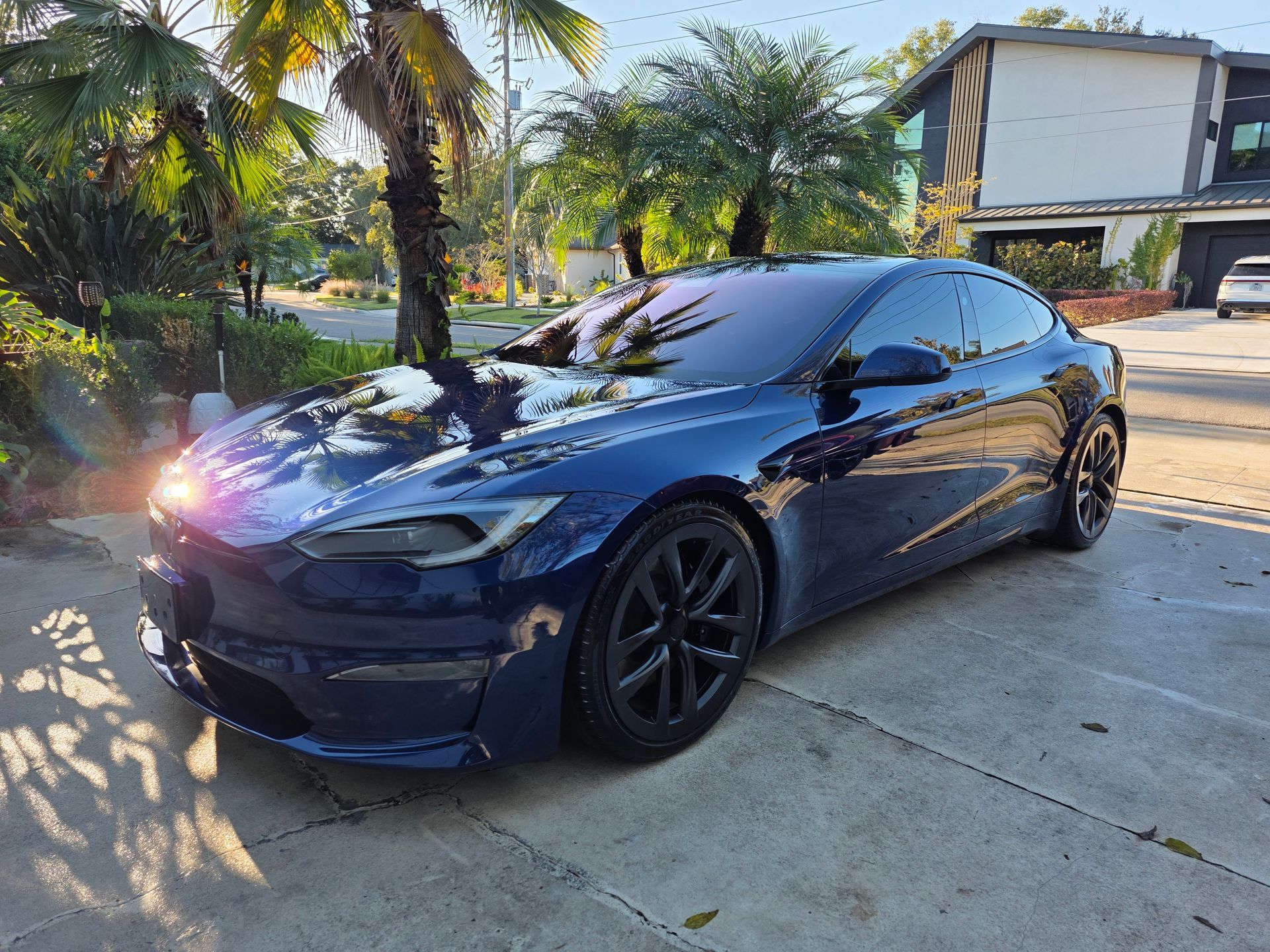Blue Tesla car parked in a driveway in front of a house.