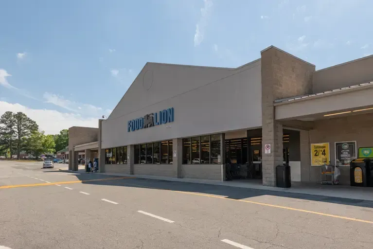 Street with shops and outdoor seating; palm trees and cars are visible.