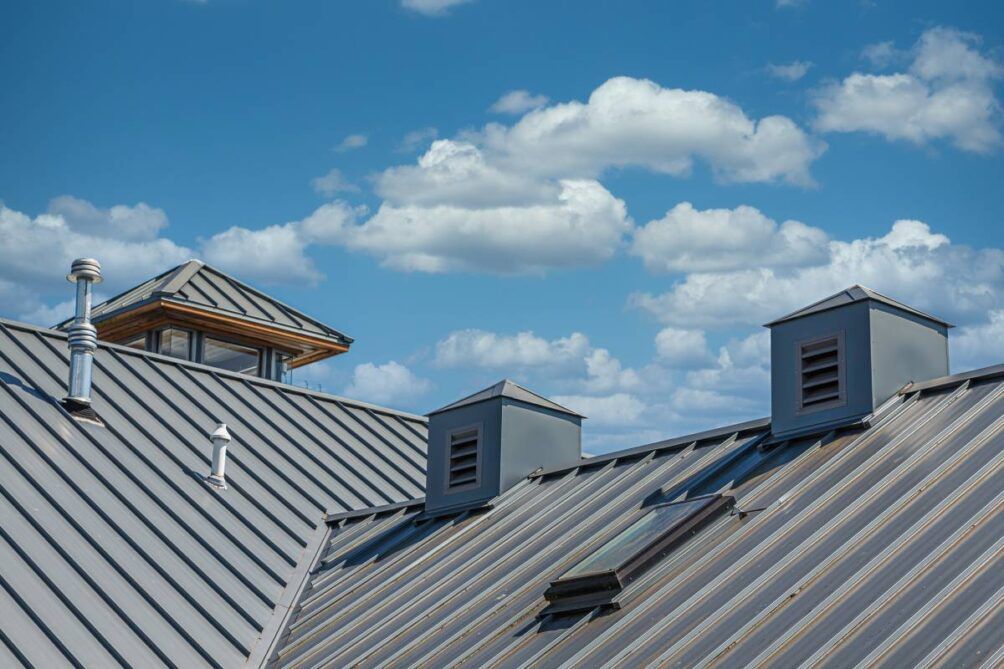 Metal roof with skylights and vents against a blue sky with fluffy clouds.