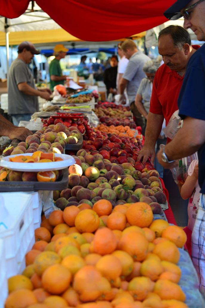 Farmer's Market fruit stand with bright fruit on table and shoppers picking and choosing