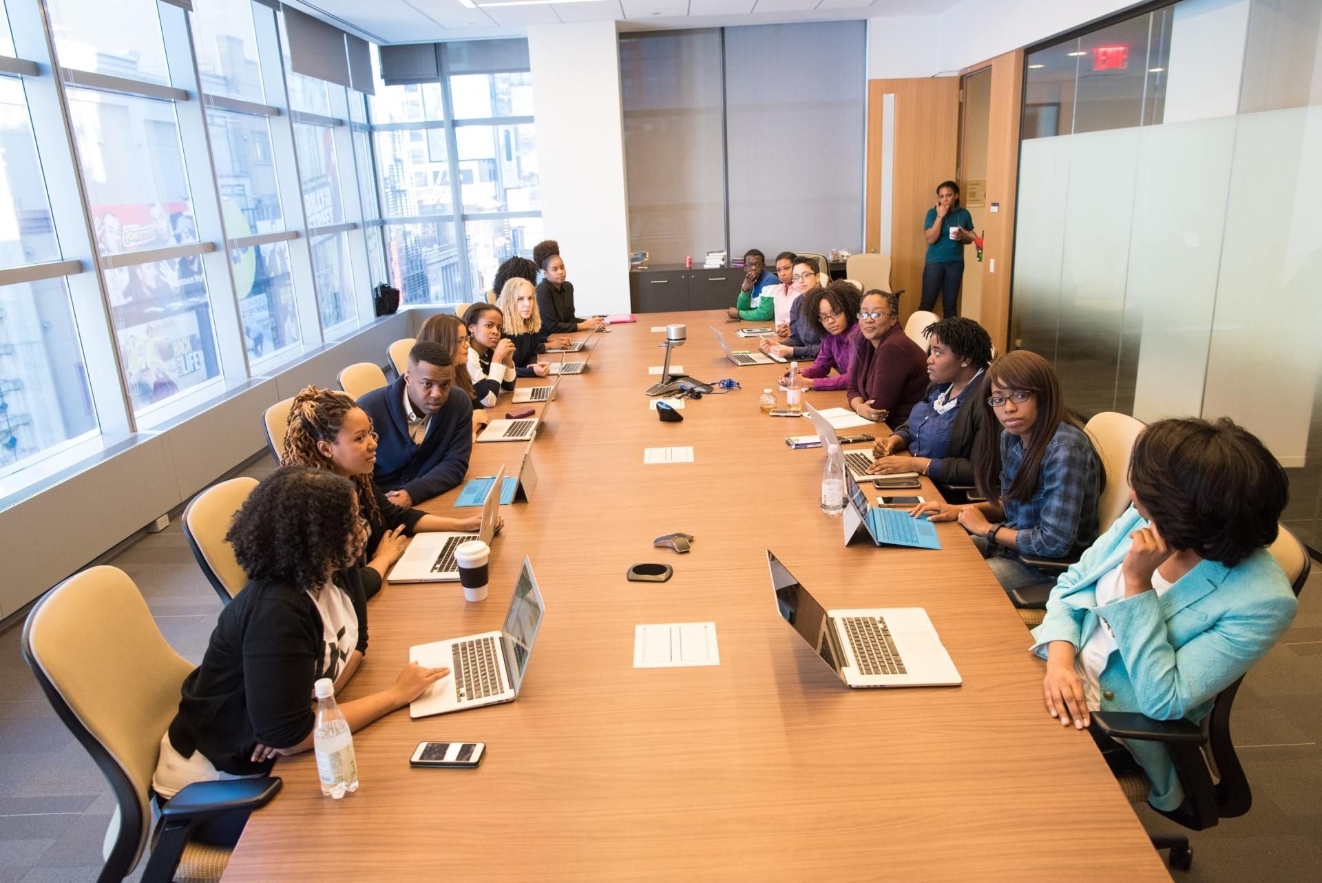 A group of people are sitting at a long table with laptops.
