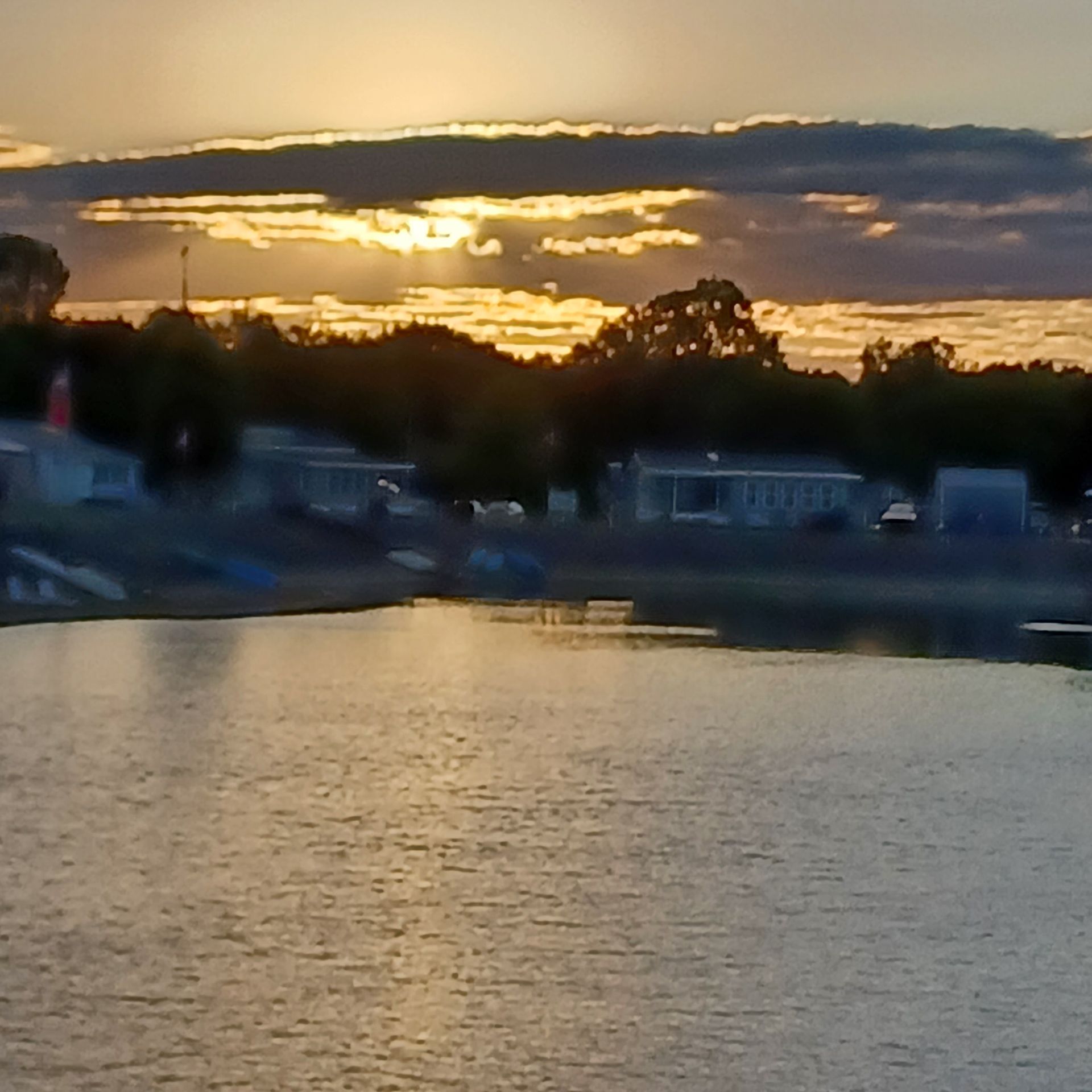 A sunset glows over a lake with silhouettes of trees and buildings on the distant shoreline.